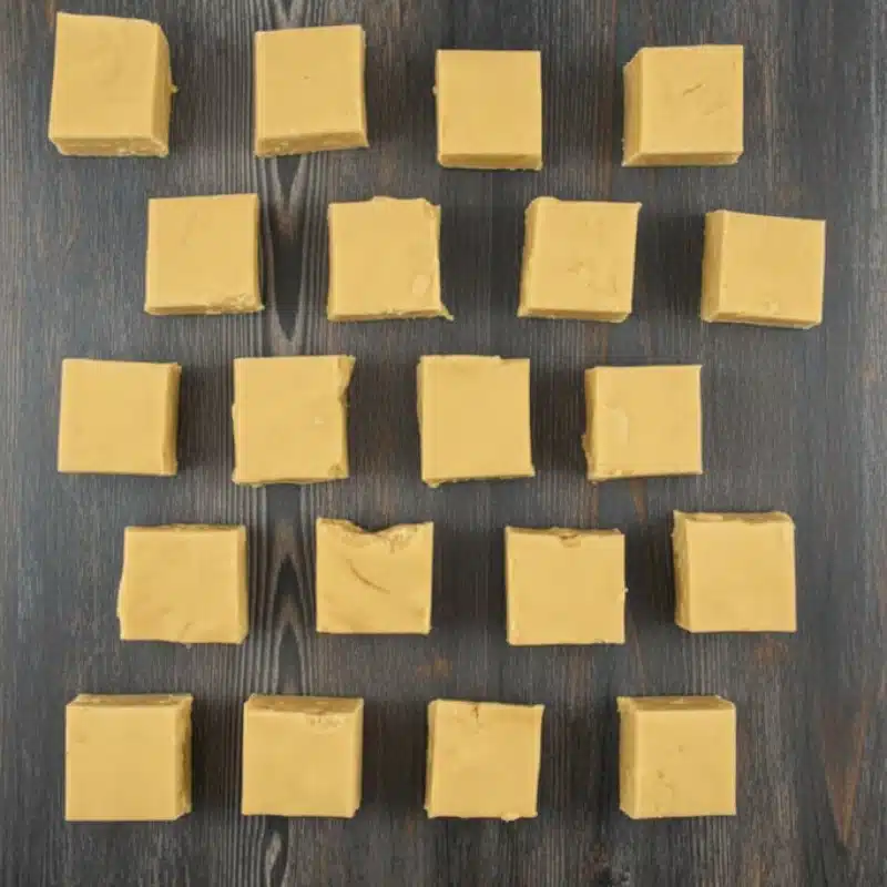 Set 3-ingredient peanut butter fudge cut into 16 even squares and arranged on a wooden surface.