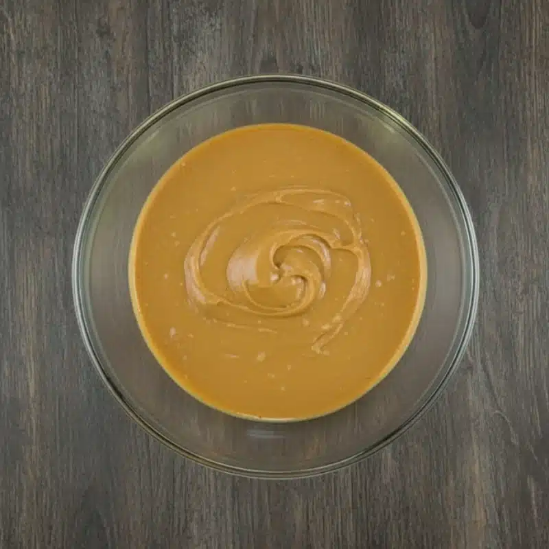 Melted butter and peanut butter stirred into a smooth, creamy mixture in a glass bowl.