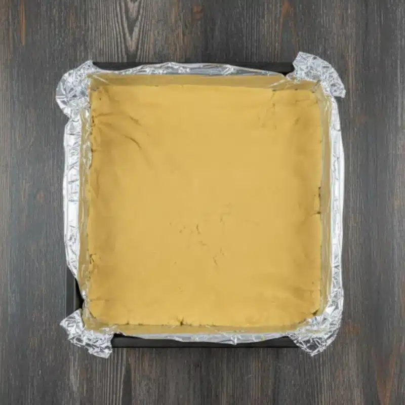 Peanut butter fudge mixture spread evenly into a foil-lined square baking pan before setting.