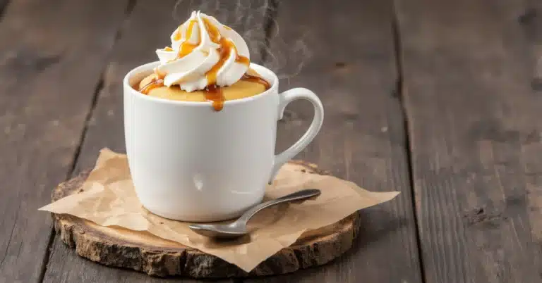 Warm vanilla mug cake (no egg) with melted caramel sauce and whipped cream, photographed on a dark wooden surface.